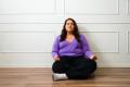 Woman with long, dark hair in a purple sweater and black leggings sitting on the ground doing breathing exercises