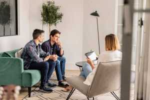 Two men sitting on a green couch speaking to a couples therapist