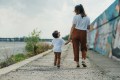 A mother and son are walking down a sidewalk holding hands, looking at each other