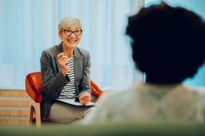 A cheerful psychotherapist is sitting in the office with a client and having a successful session where the patient is having a breakthrough in response to one of the therapist's questions.