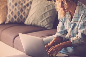 Woman working online with laptop computer comfortably sitting on the sofa at home