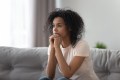 Young woman sitting on couch looking off in the distance, looking anxious and scared, navigating thoughts of OCD.