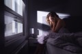 Woman with insomnia sitting up in bed as the light comes in, head in hands tired from not sleeping
